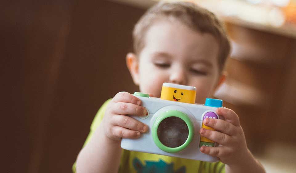 the boy holds a toy camera in his hand and looks at it